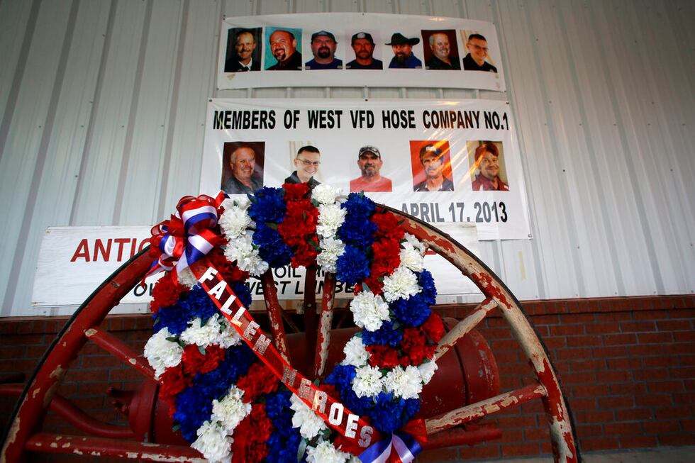 A photo montage has a wreath of flowers placed in front of it on the exterior wall of the...
